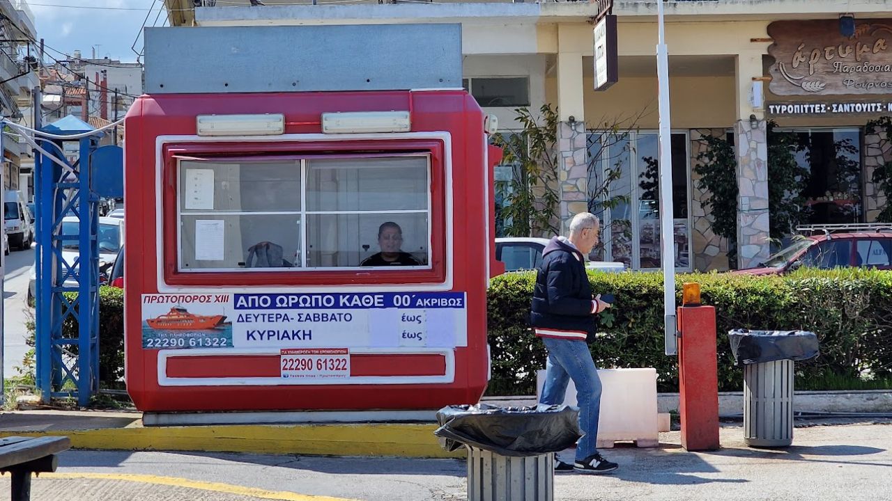 red ticket booth at the port of Skala Oropou with a timetable notice and a picture of a red ferry