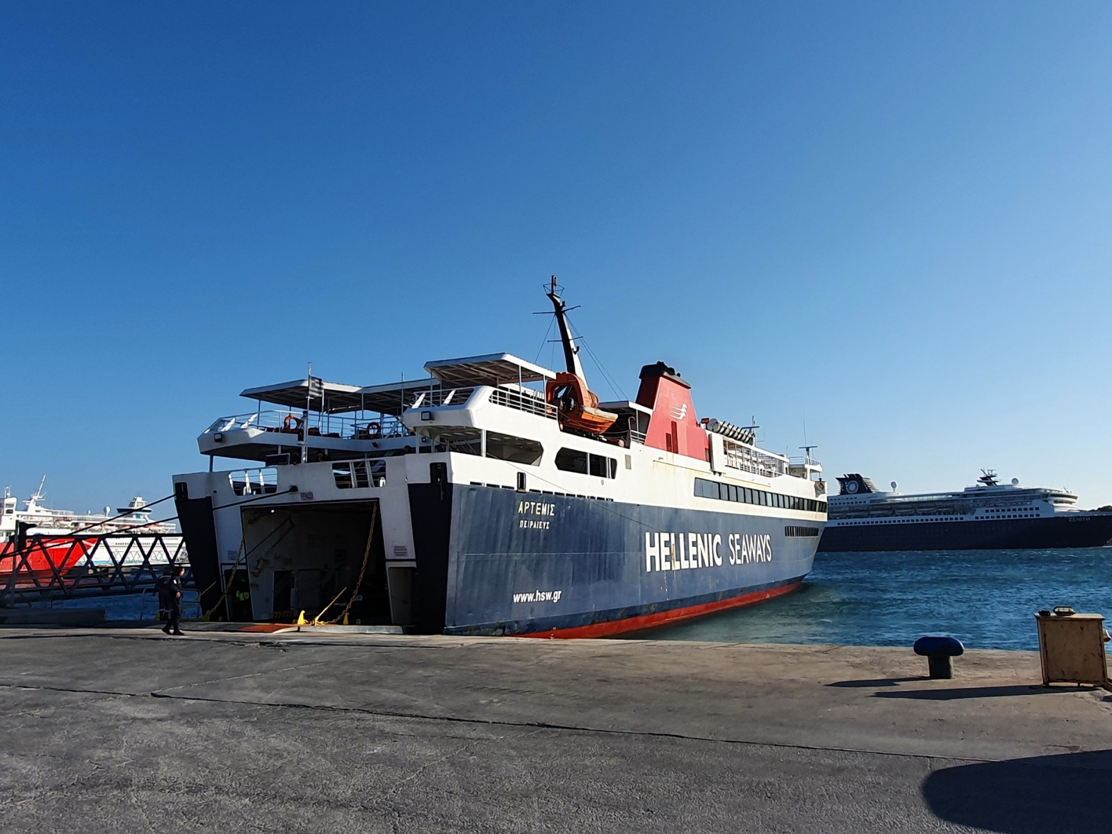 Artemis, a Hellenic Seaways car ferry with a dark blue hull and white superstructure, moored stern-to at the dock with her vehicle ramp down on a clear day.