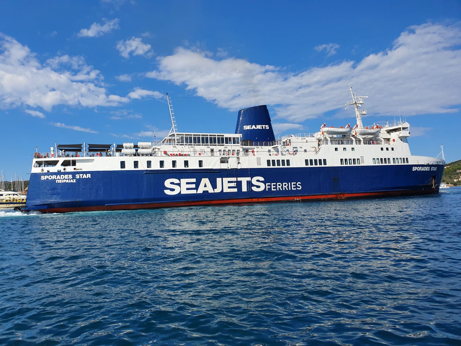 The Seajets ferry Sporades Star under way, seen from the side: a blue hull with SEAJETS FERRIES in large white letters, a white superstructure with a glazed lounge on the upper deck, a blue funnel marked SEAJETS and a red band at the waterline.